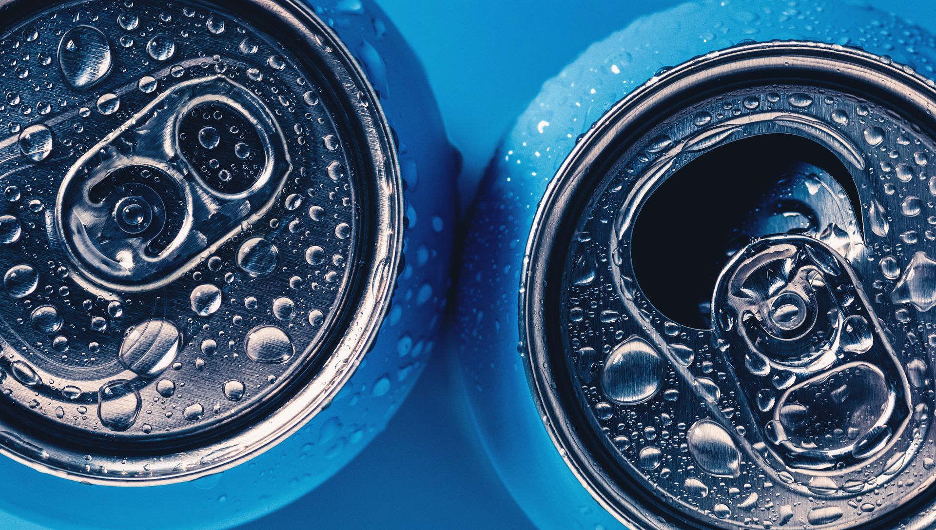 Two silver soda can tops with water droplets on a bright blue background