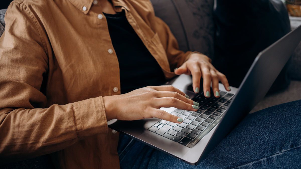 Person typing on a laptop while seated indoors, wearing a tan jacket and jeans.