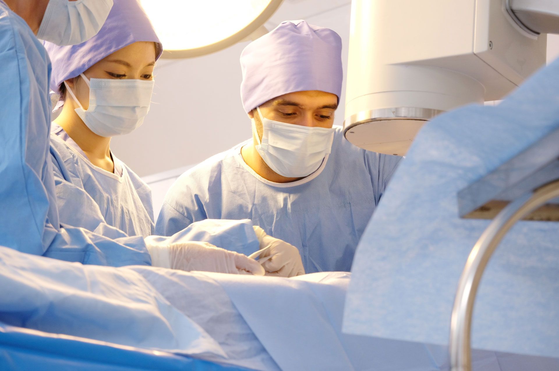 Surgeons in blue scrubs and masks performing an operation in an operating room