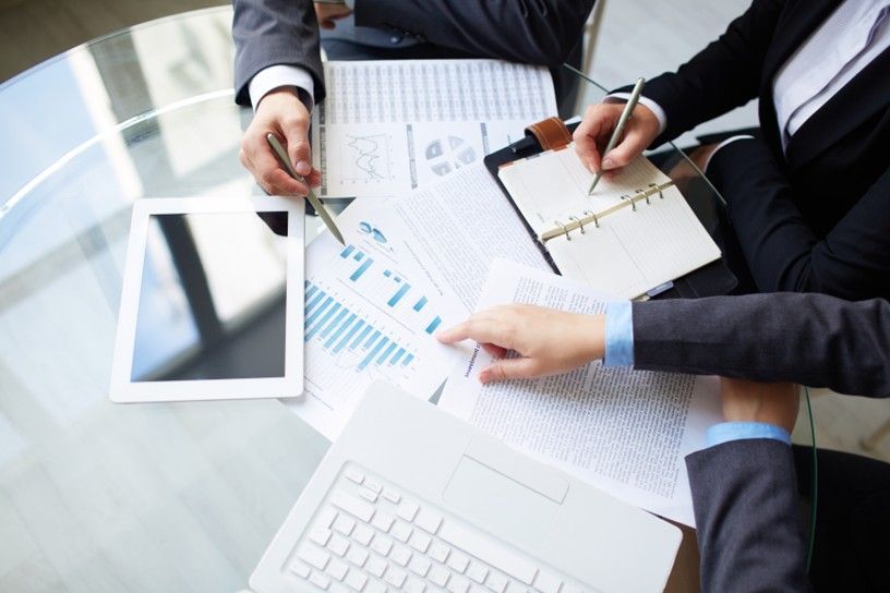 Colleagues reviewing charts and graphs at a desk with a tablet and laptop
