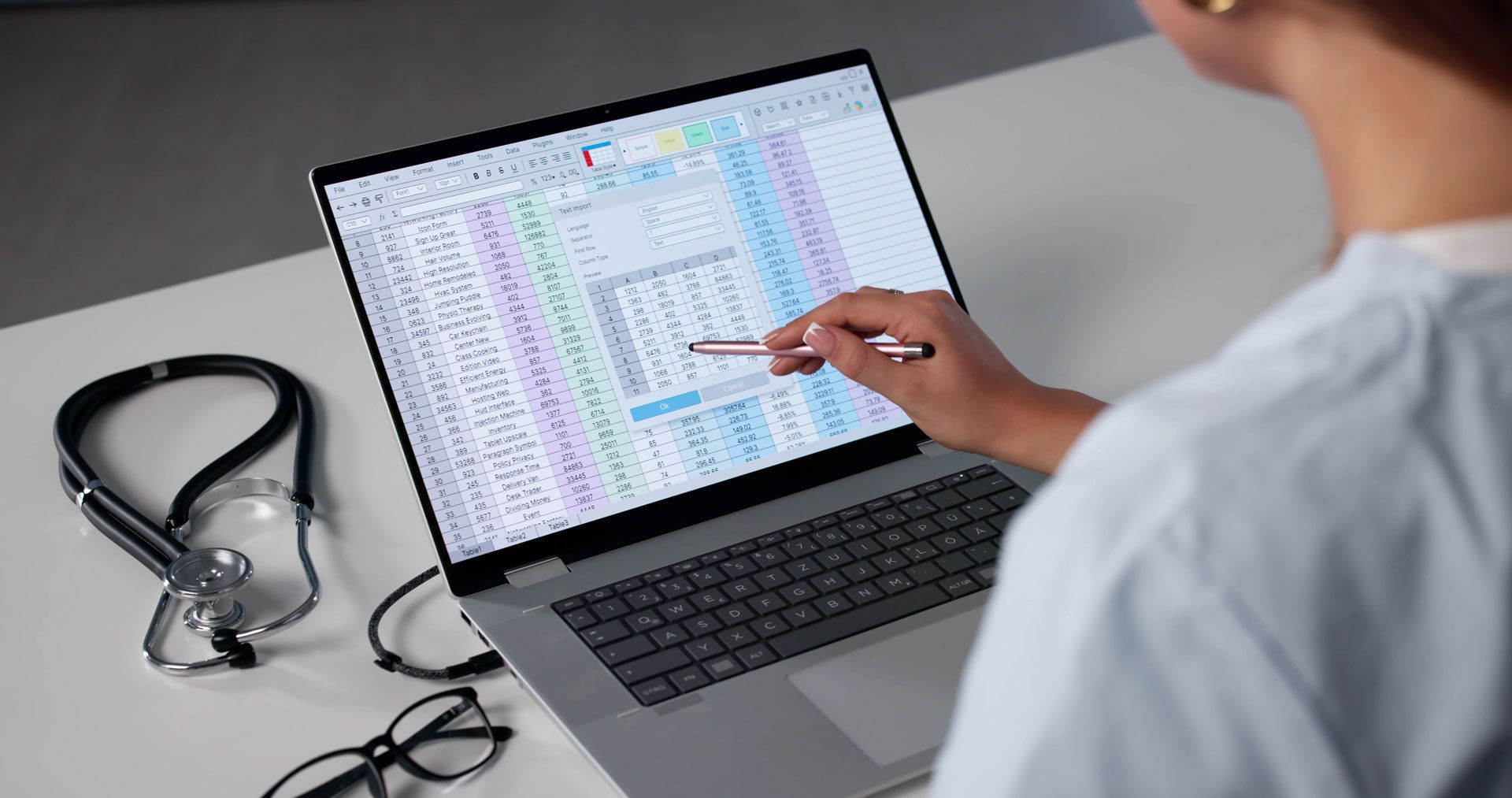 Medical professional pointing at a laptop screen with patient data beside a stethoscope