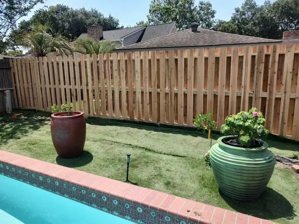 A wooden fence surrounds a swimming pool in a backyard.