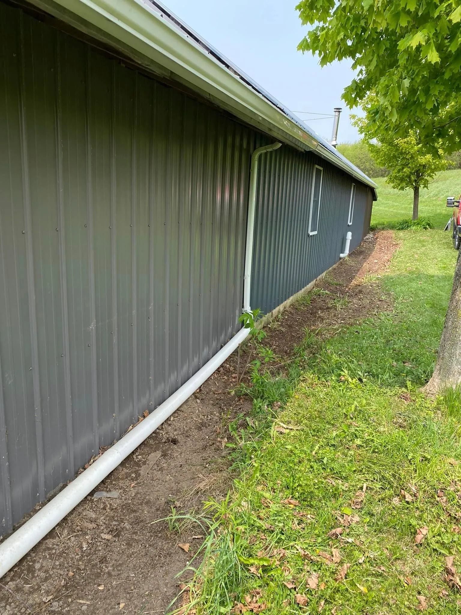 Gray metal building with white gutters and downspouts, next to a grassy area.