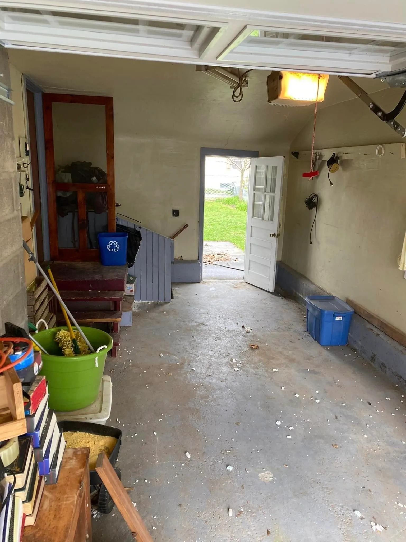 Inside of garage, looking towards a door. Items like buckets, stairs, and tools on left, right, and foreground.