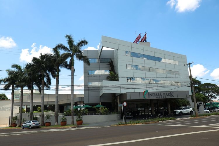 Prédio de escritórios moderno e branco com palmeiras e estacionamento sob um céu azul.