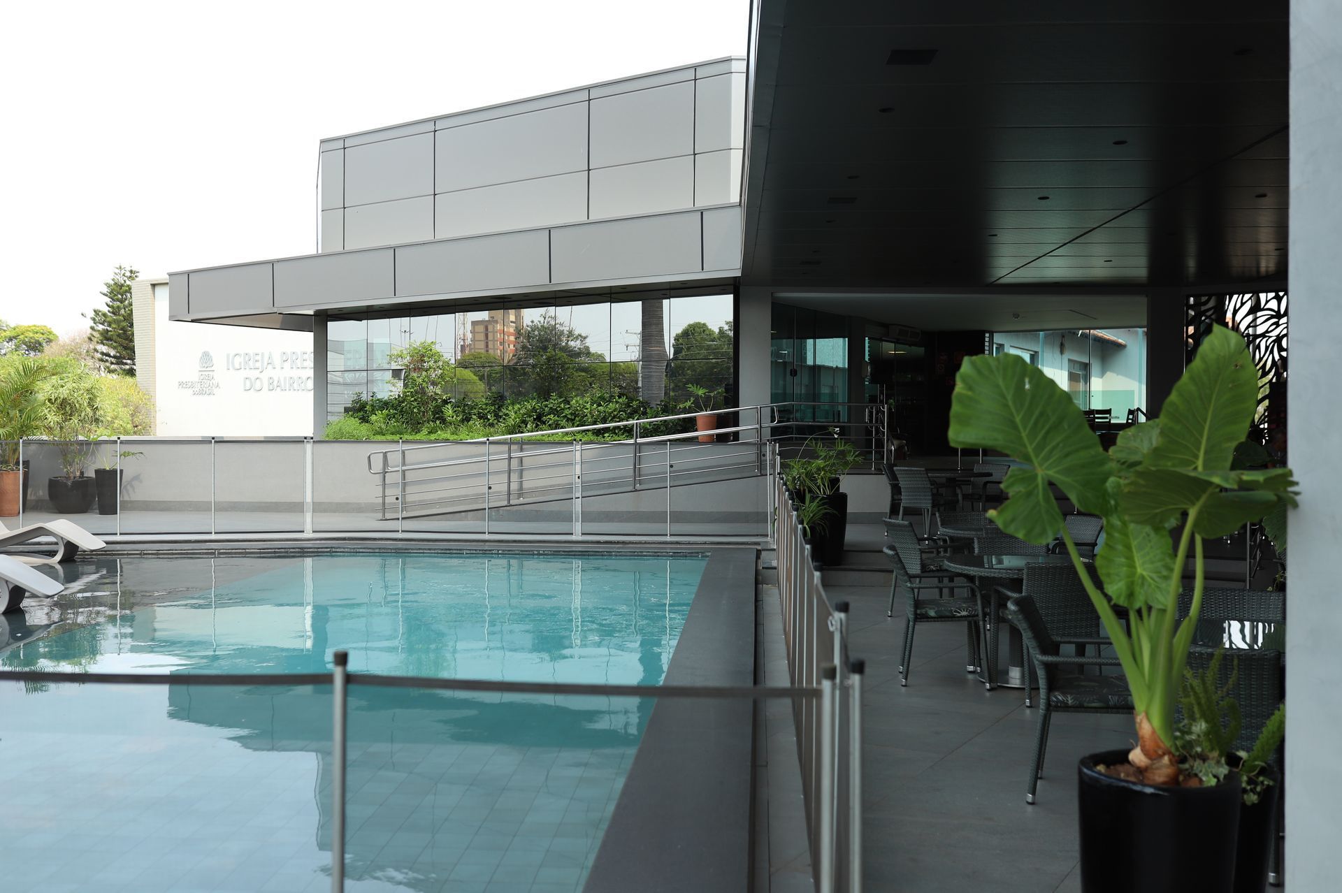 Piscina moderna na cobertura ao lado de um lounge com paredes de vidro e área de estar com vasos de plantas.