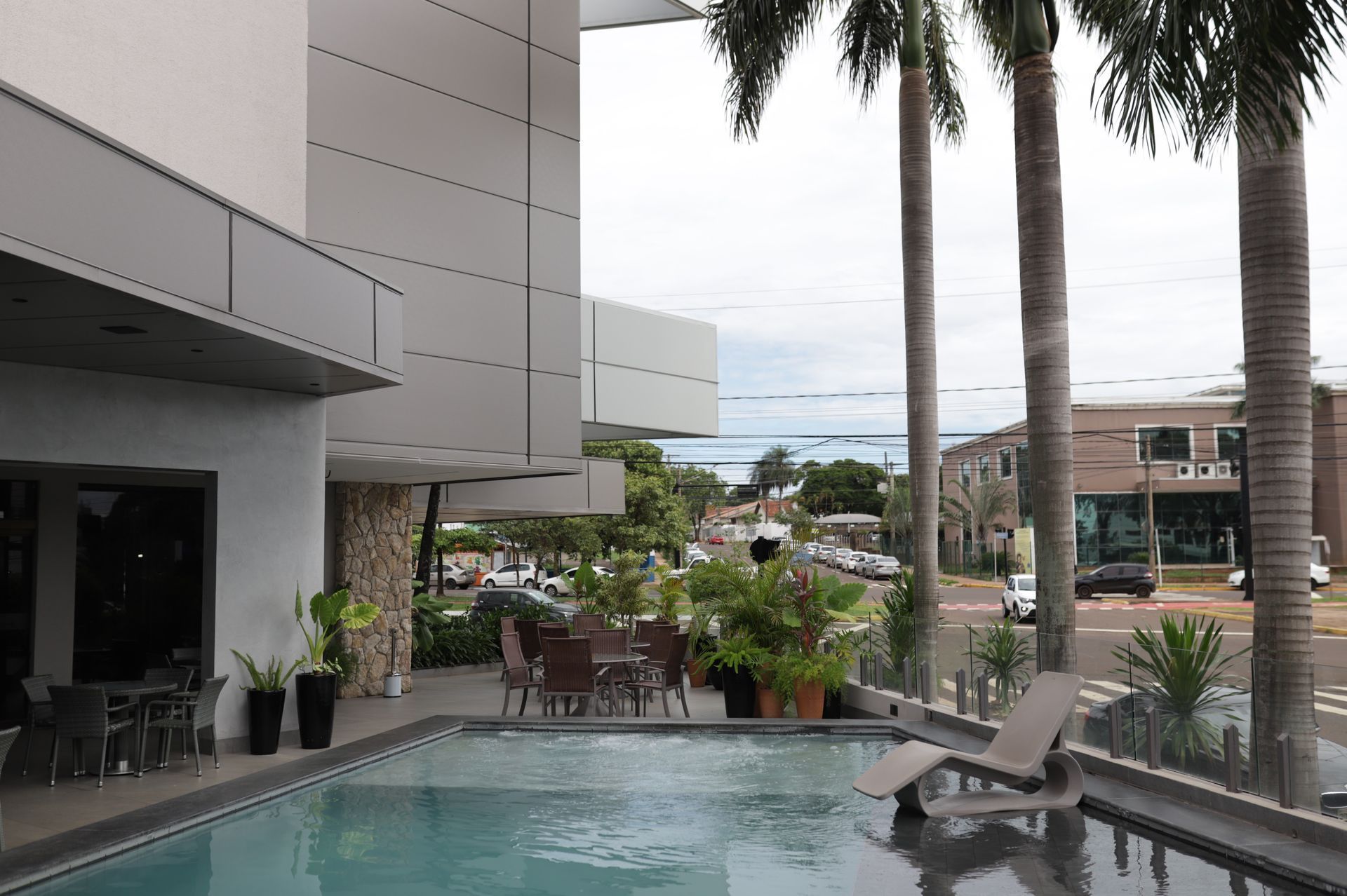 Pátio moderno de resort com uma pequena piscina, espreguiçadeiras, plantas em vasos e palmeiras com vista para a água.