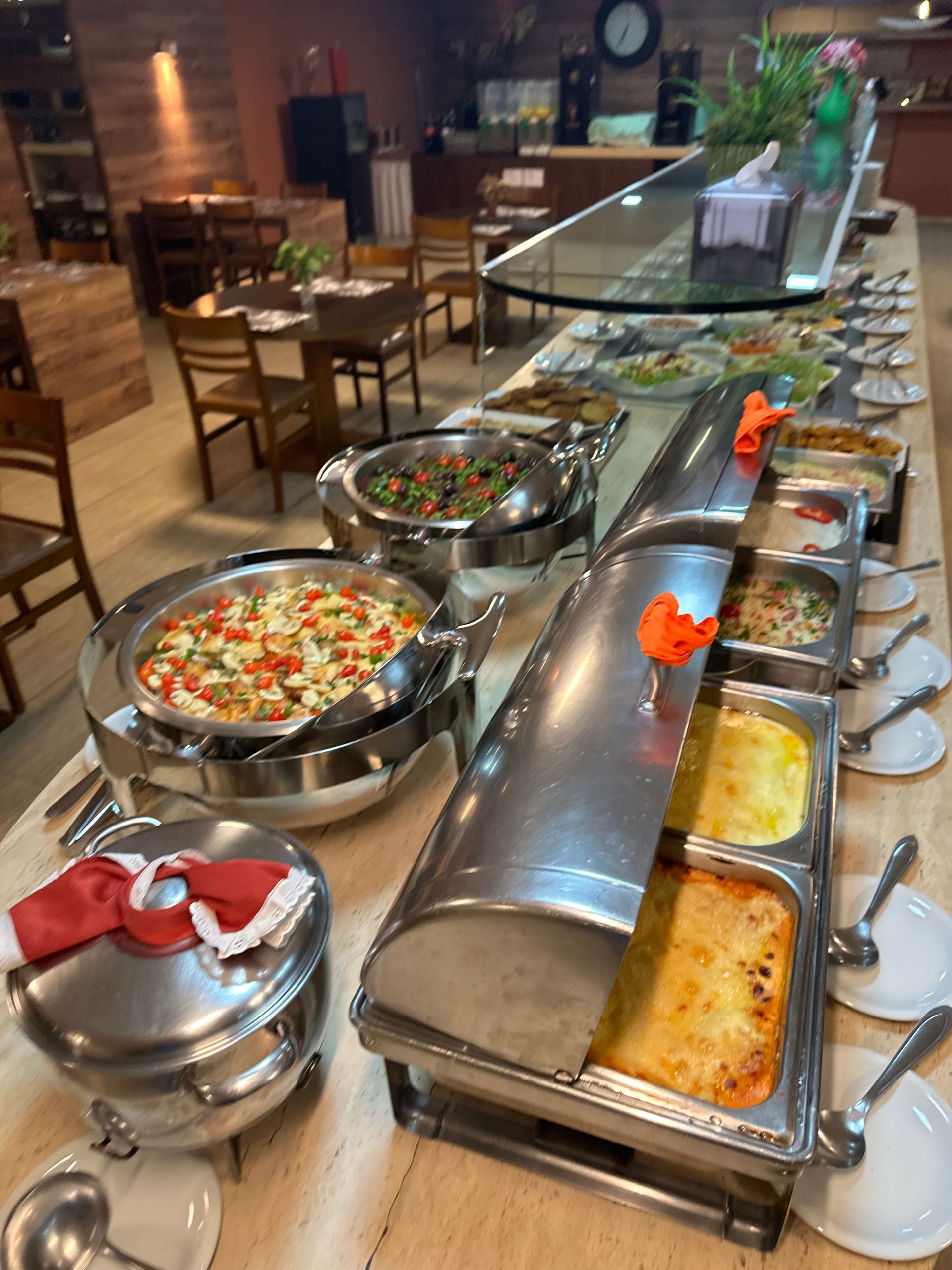 Mesa de buffet com diversos pratos quentes em um salão de jantar de restaurante.