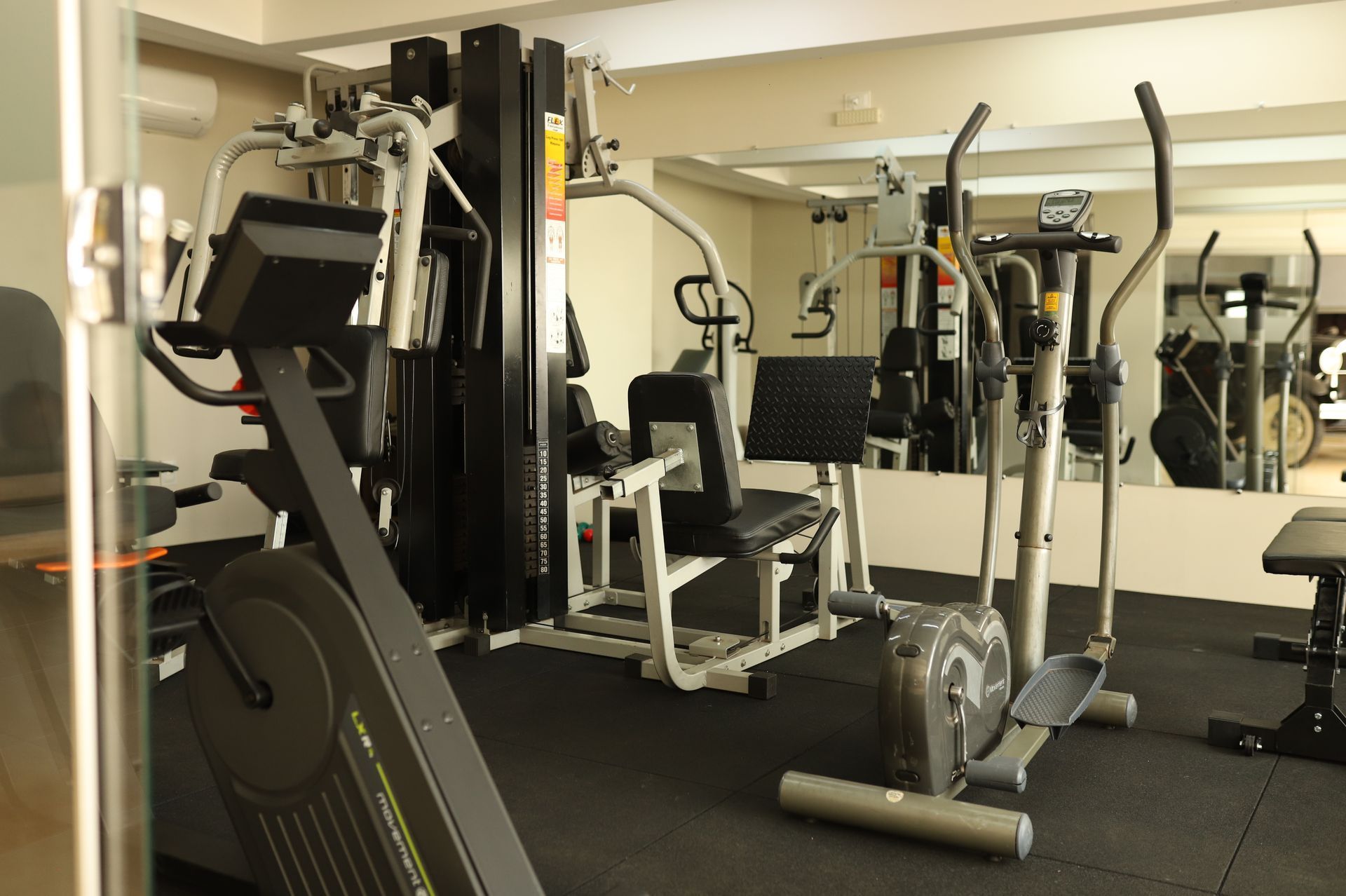 Interior de academia com aparelhos de ginástica, espelhos e equipamentos em preto e prata sobre piso de borracha.