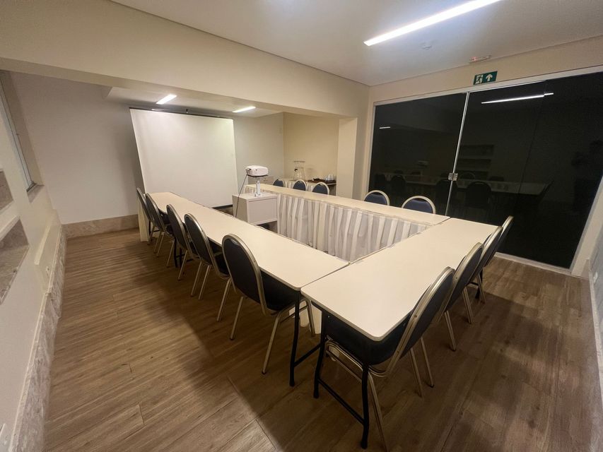 Arranha-céu alto iluminado à noite, com um restaurante no terraço e luzes da cidade ao redor.