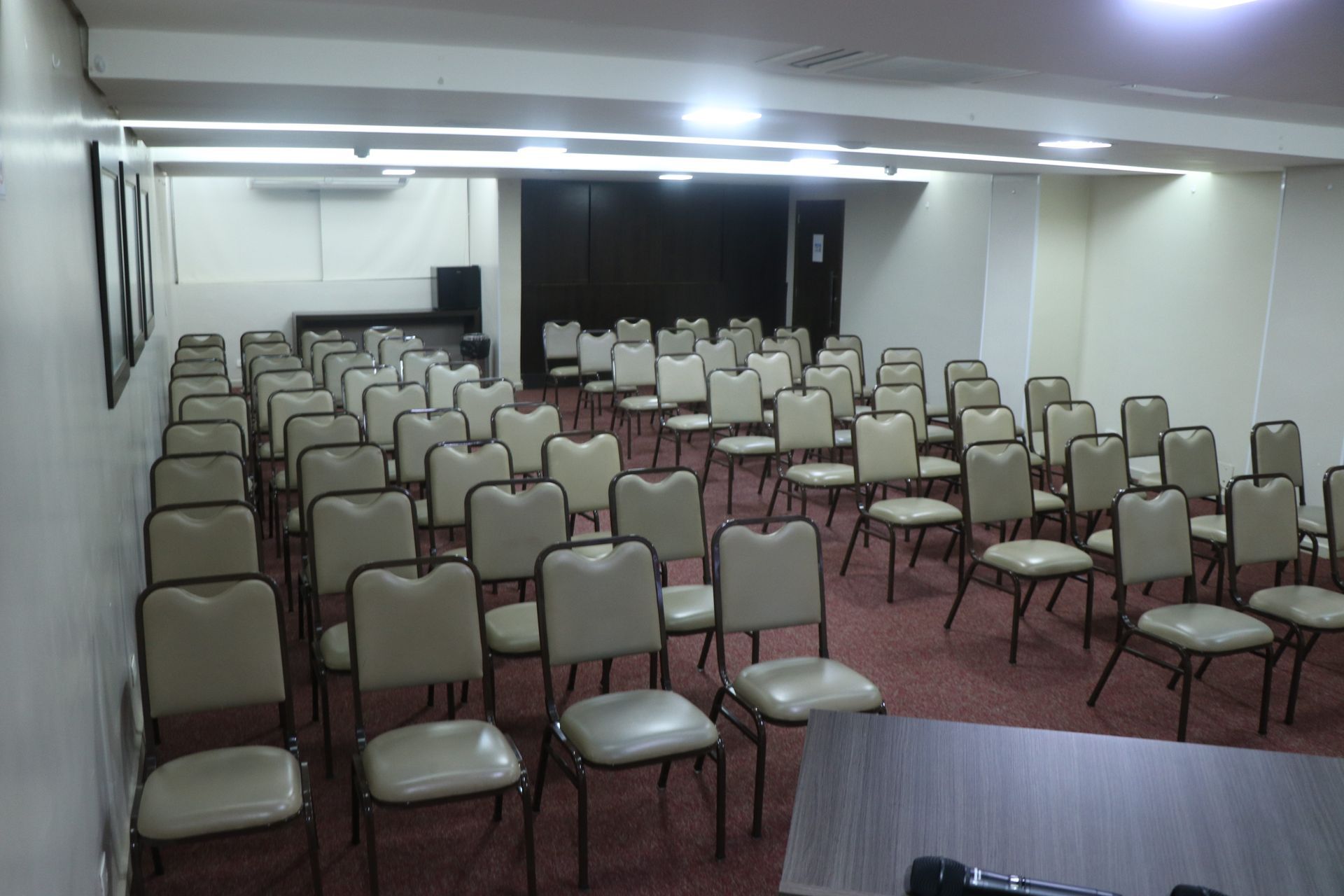 Sala de conferências vazia com fileiras de cadeiras bege voltadas para a frente.