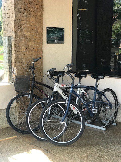 Três bicicletas estacionadas ao lado de um prédio de tijolos perto de uma porta de vidro.
