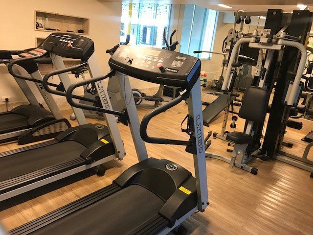Academia interna com esteiras, máquina de remo e equipamentos de musculação em piso de madeira.