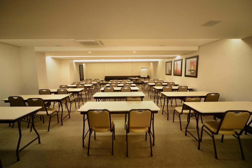 Sala de conferências com fileiras de mesas e cadeiras sob iluminação aconchegante.