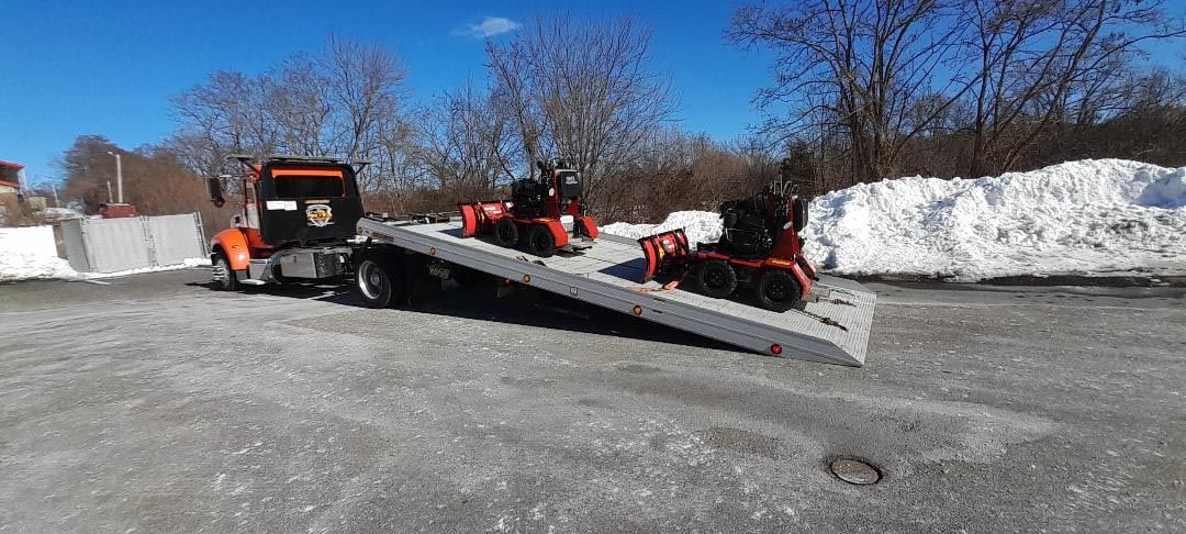 A tow truck is carrying a lawn mower on a ramp.
