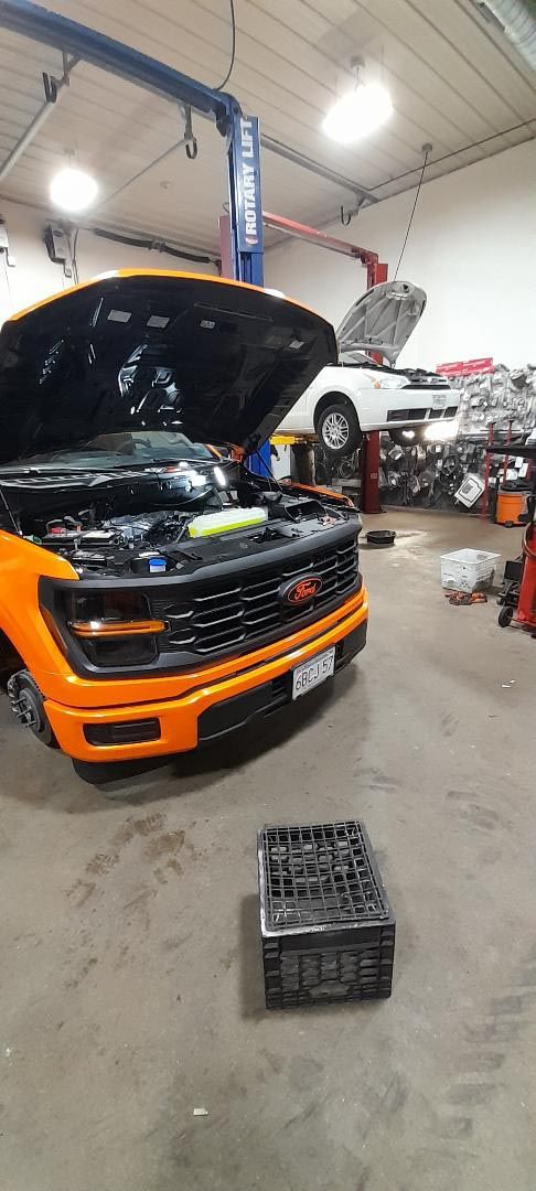 An orange truck is parked in a garage with its hood open.