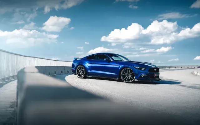 Blue sports car on a rooftop track under a bright sky with clouds