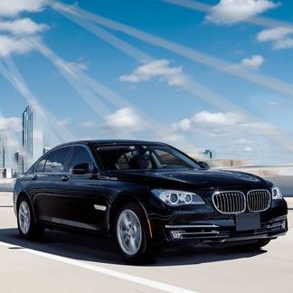 Black BMW sedan driving on a bridge under a blue sky with clouds