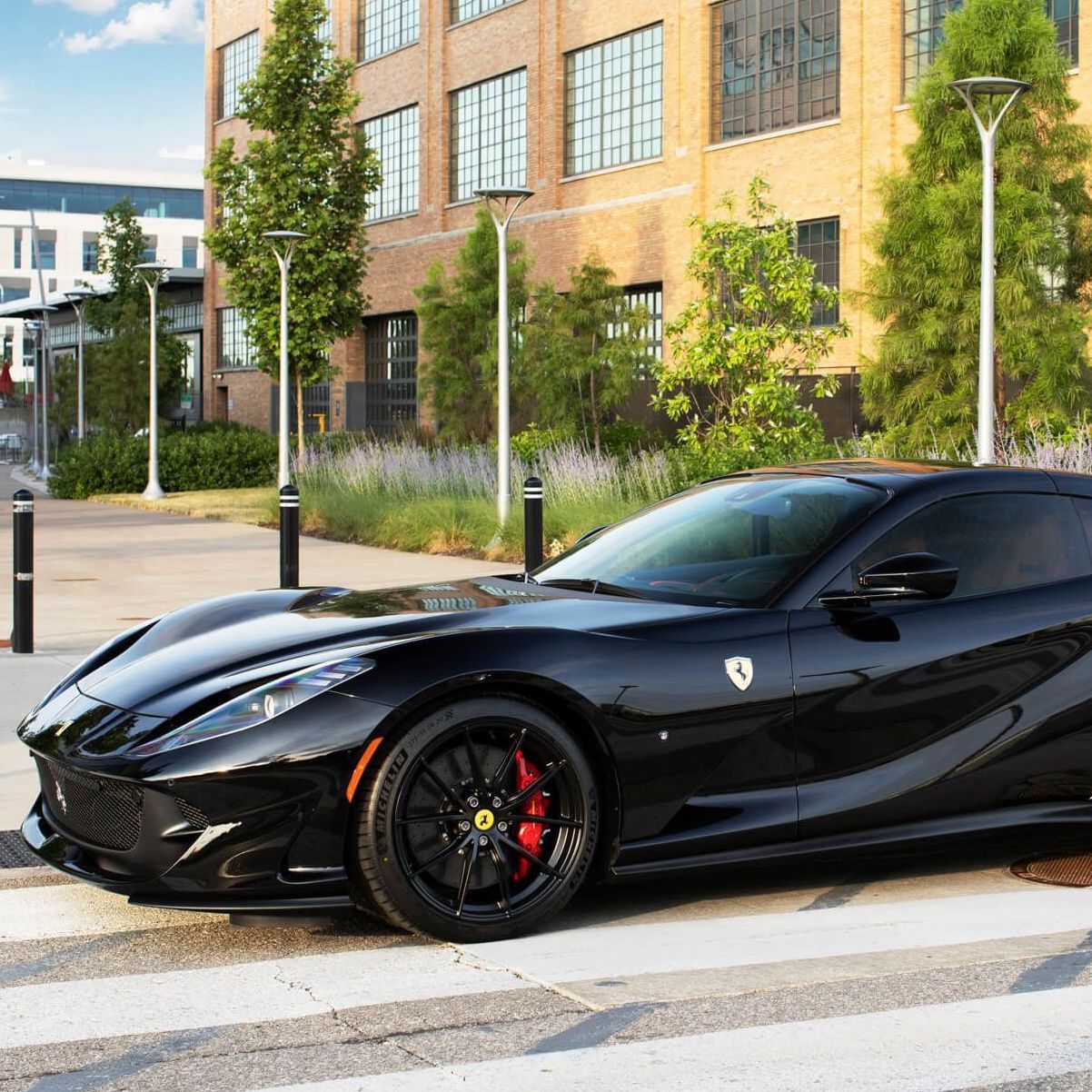 Black sports car parked on a city street beside a brick building and trees