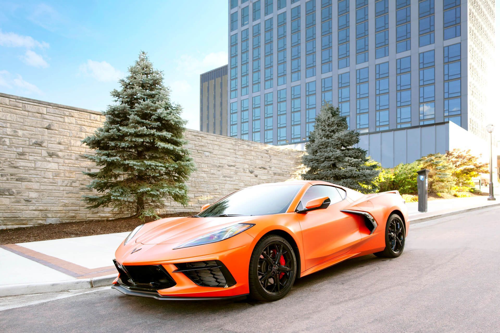 Orange sports car parked on a city street beside a modern building and trees