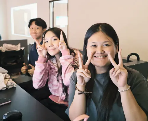 Three people smiling and making peace signs at a table in a bright room