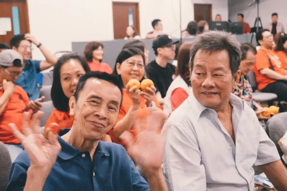 Two smiling people waving in a crowded indoor meeting room