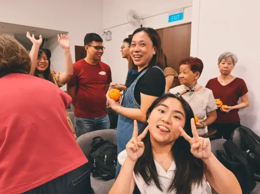 People in a room smiling and posing together, with one woman making a peace sign in the foreground.