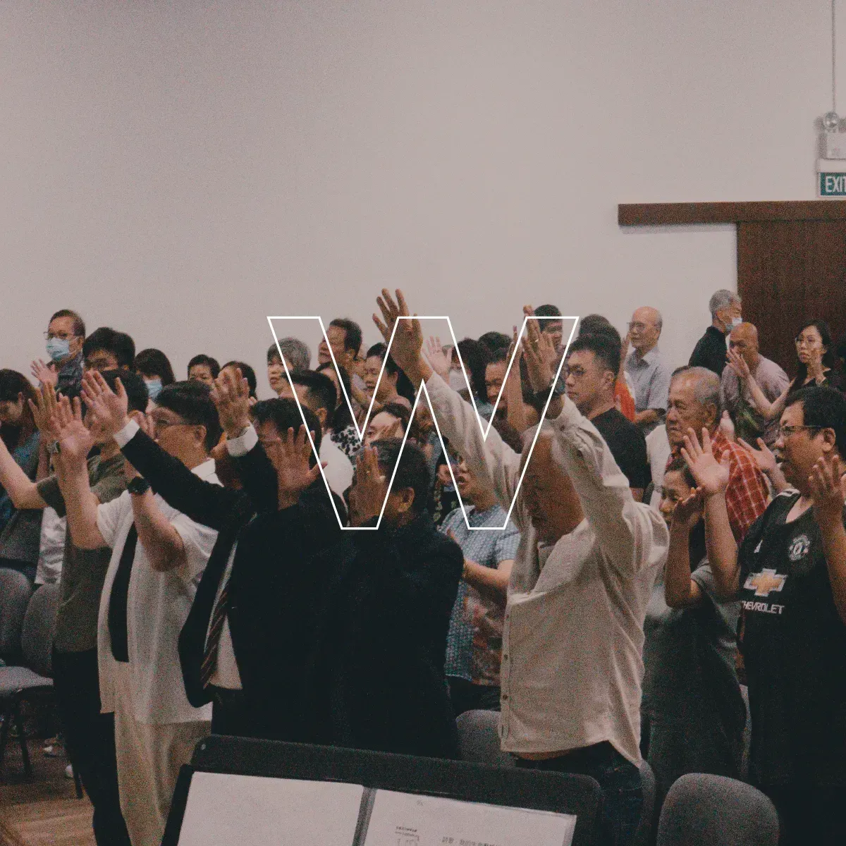 Audience standing and clapping in a hall, several people with hands raised in praise or applause