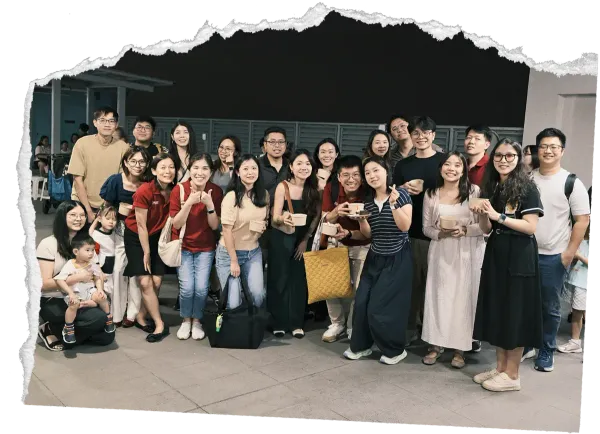 Group of people posing together outdoors, smiling in front of a building with a torn-paper style border