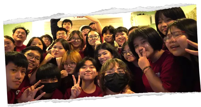 Crowded group selfie of smiling people indoors, many wearing dark red shirts and glasses.