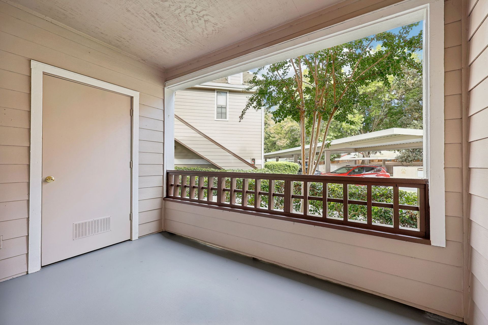 Exterior view of a patio with a door and a window overlooking a parking area with cars and trees.