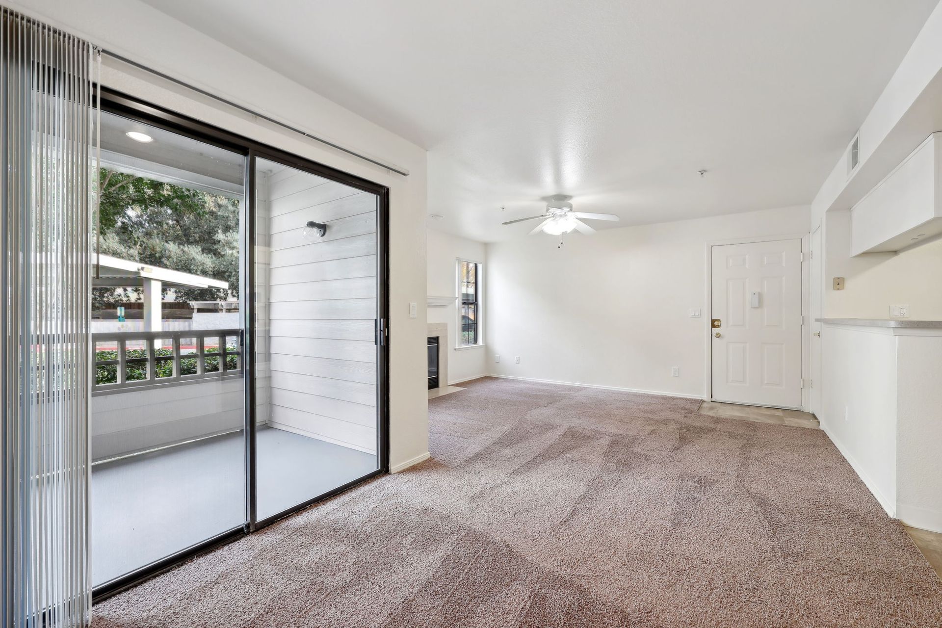 Empty living room with brown carpet, sliding door to balcony, and white walls.