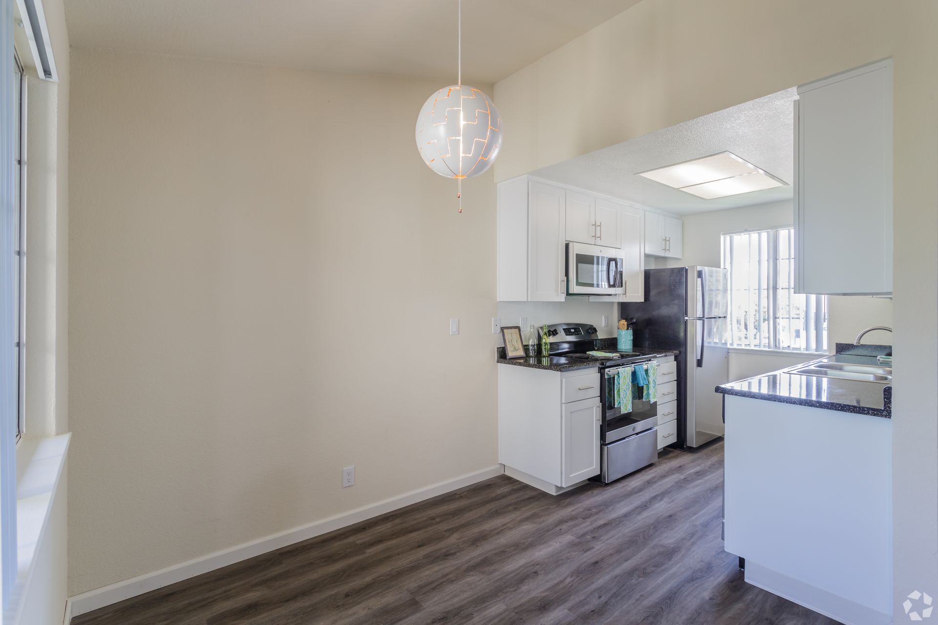 Dining area with view into a white kitchen, gray wood-look flooring, cream walls, and a white globe light.