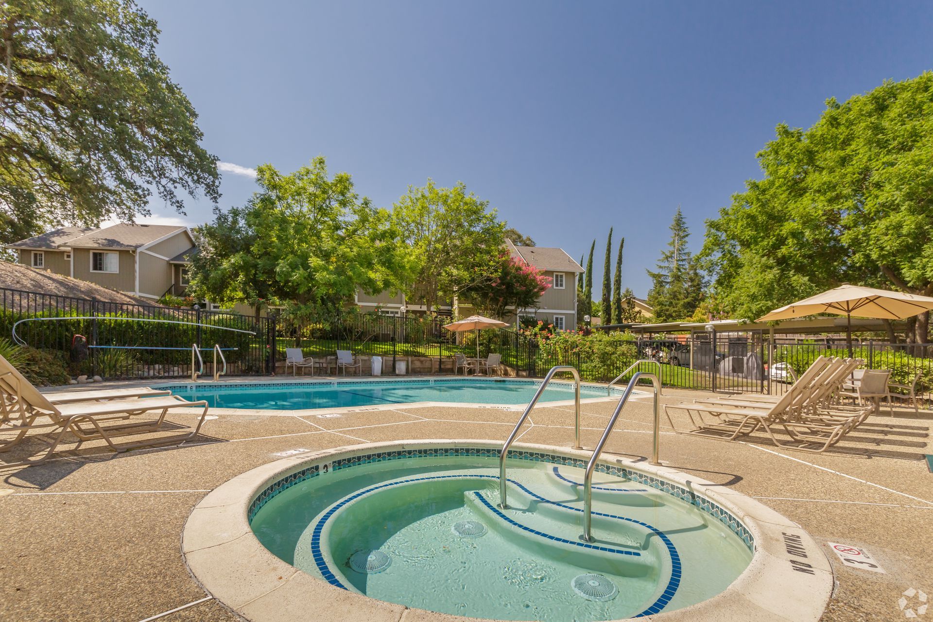 Pool and hot tub with lounge chairs on a sunny day.