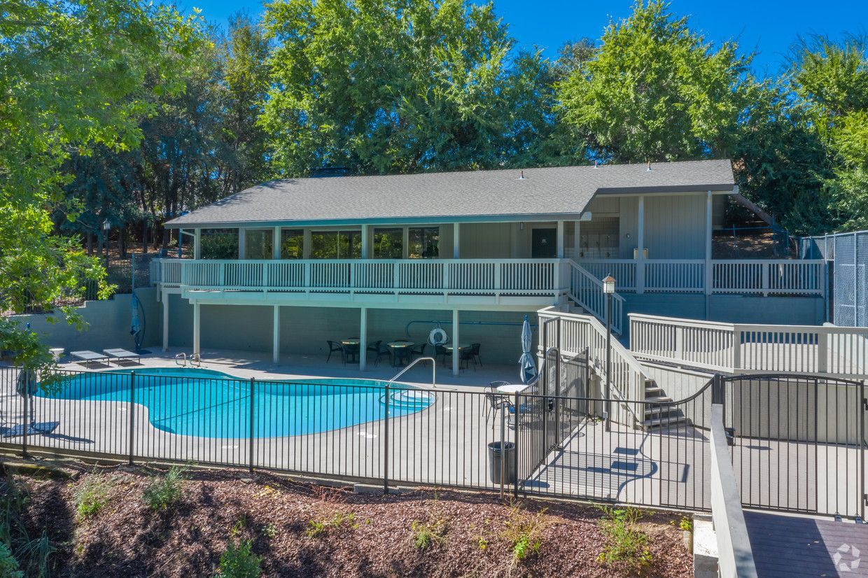 A pool with a building overlooking it, surrounded by trees. The building has a balcony and is light gray.