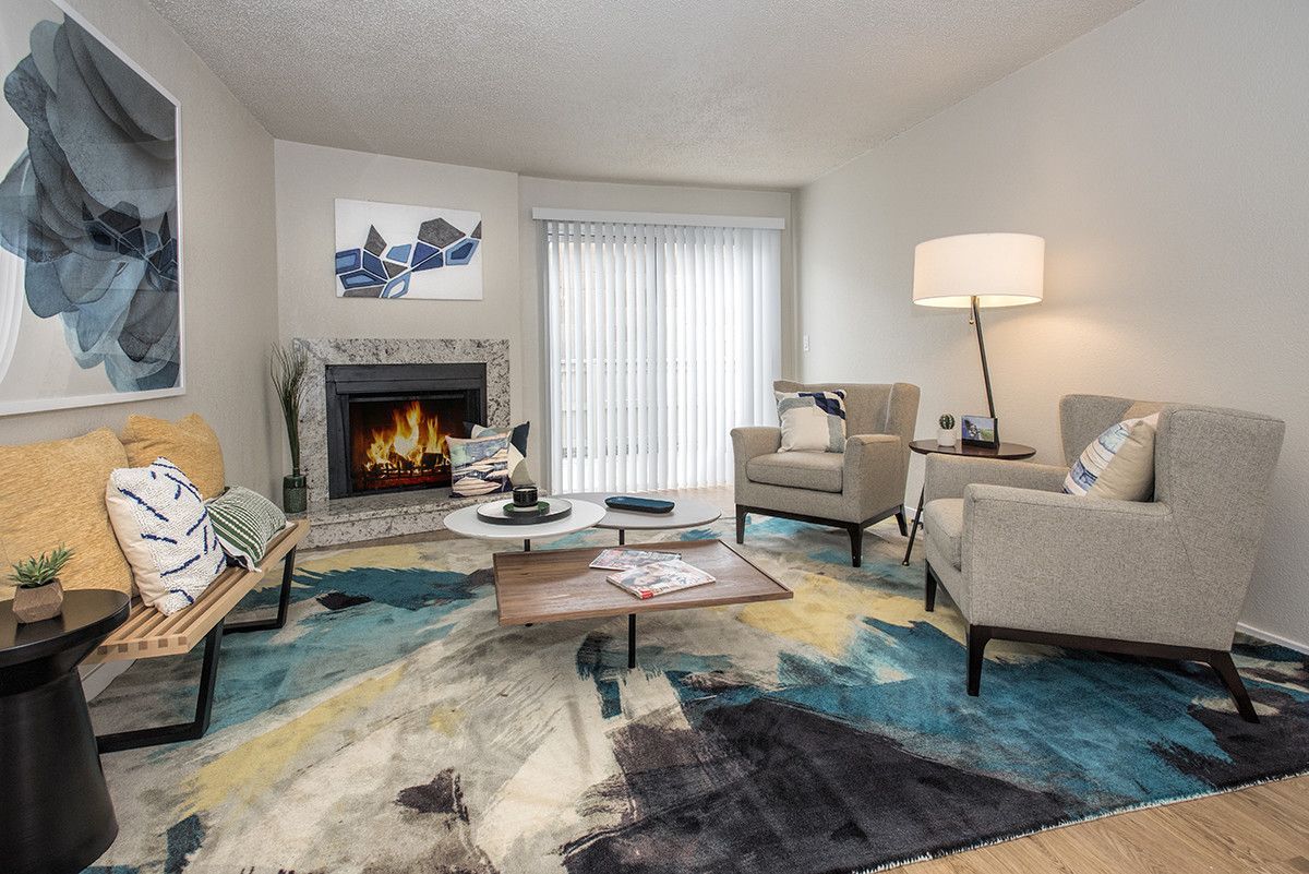 Living room with fireplace, two armchairs, a bench, and a modern colorful rug.