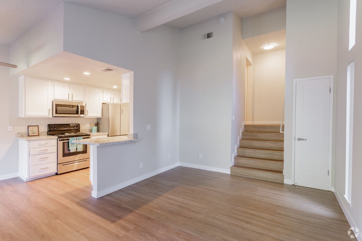 Open-concept living space with kitchen and stairs to an upper level; light wood floors, white cabinetry, and gray walls.