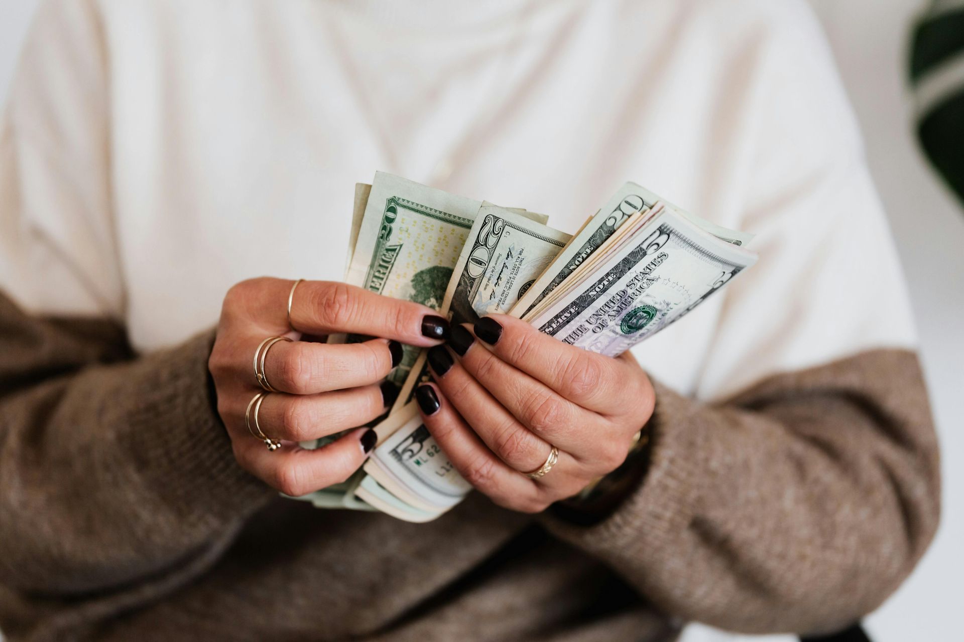 Hands counting U.S. dollar bills, with dark nail polish and rings visible.