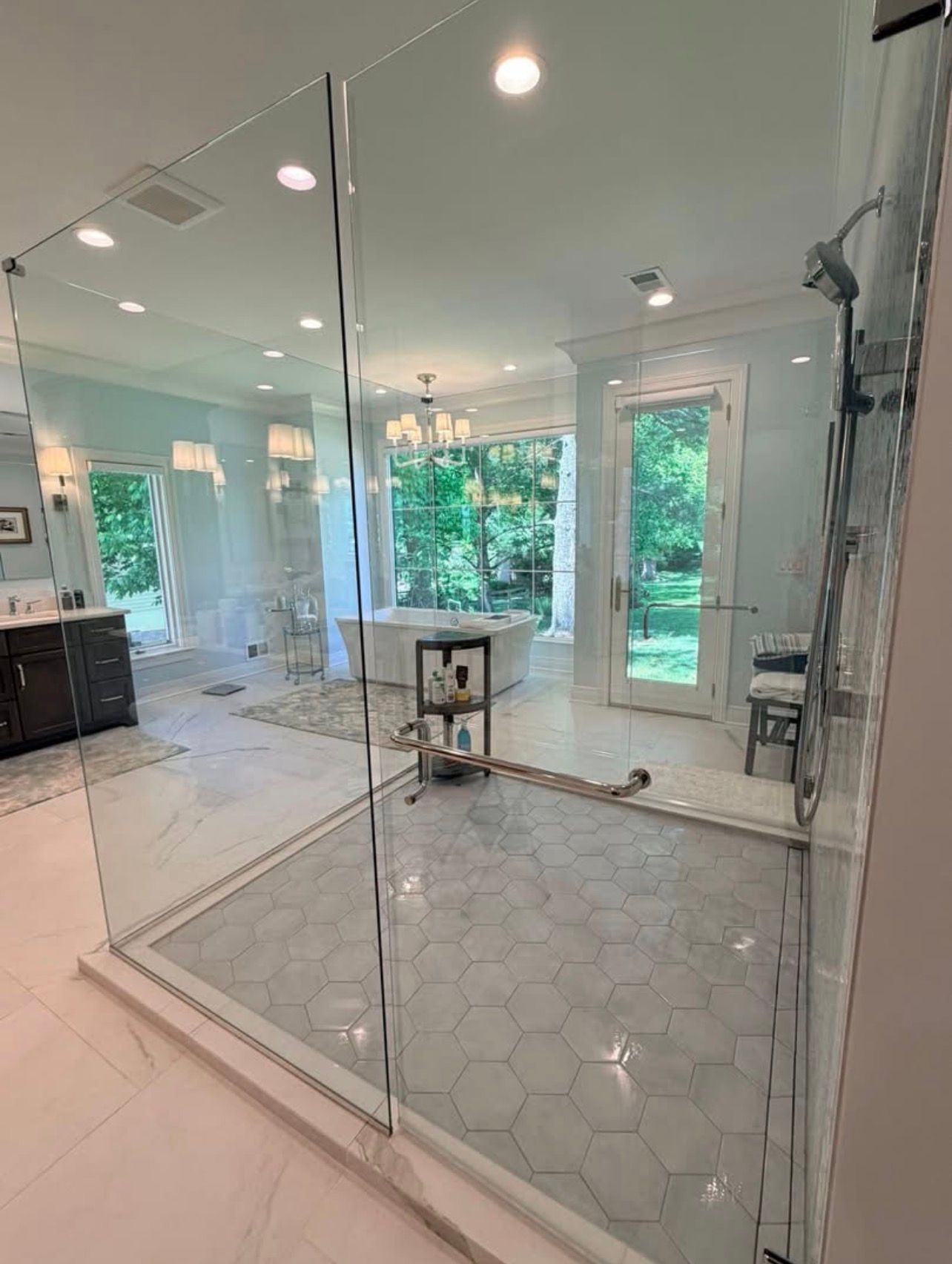 Glass shower enclosure in a bright bathroom with hex tile floor and white walls