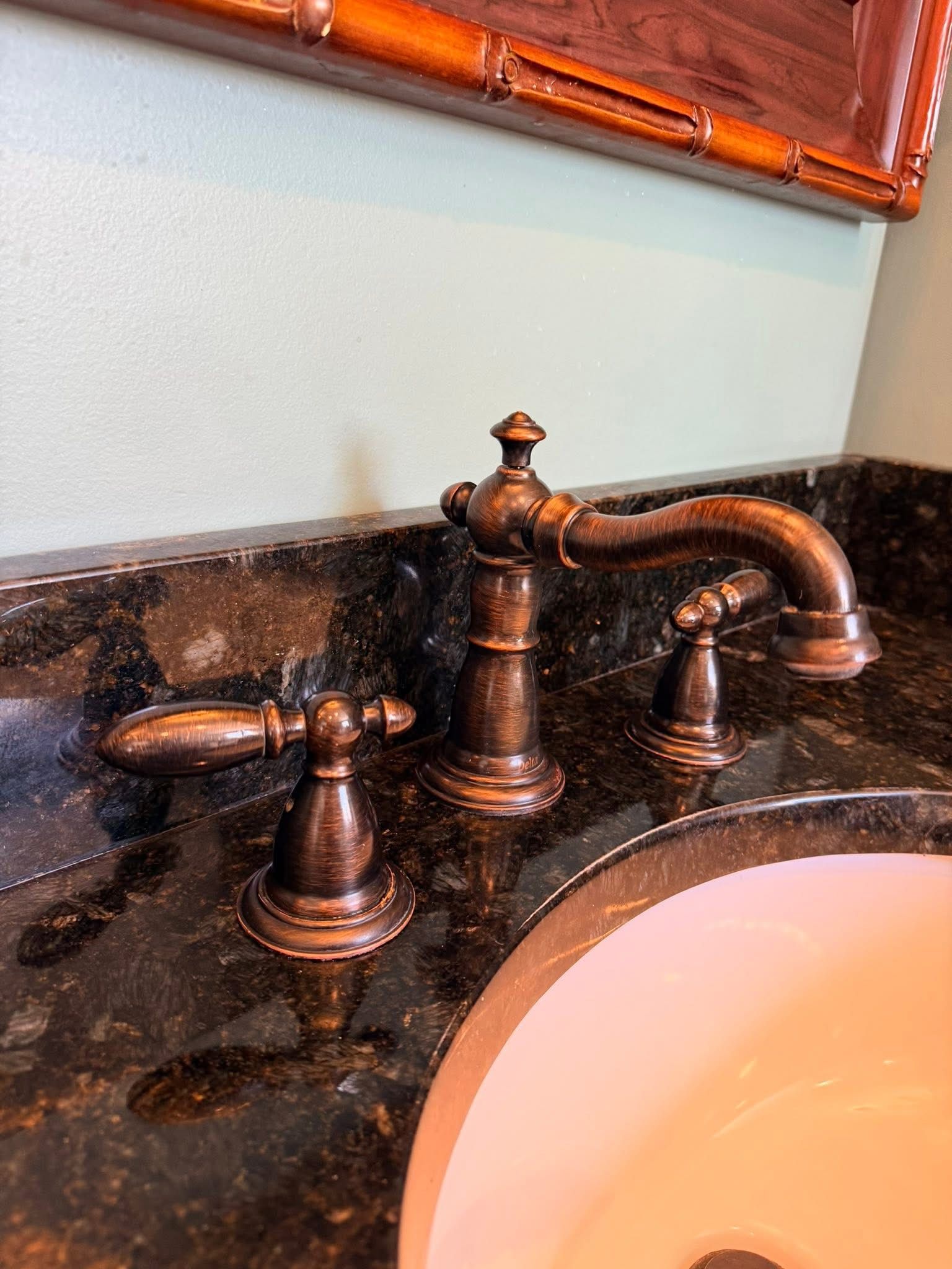 Bronze bathroom faucet with cross handles and curved spout on dark granite counter beside a white sink