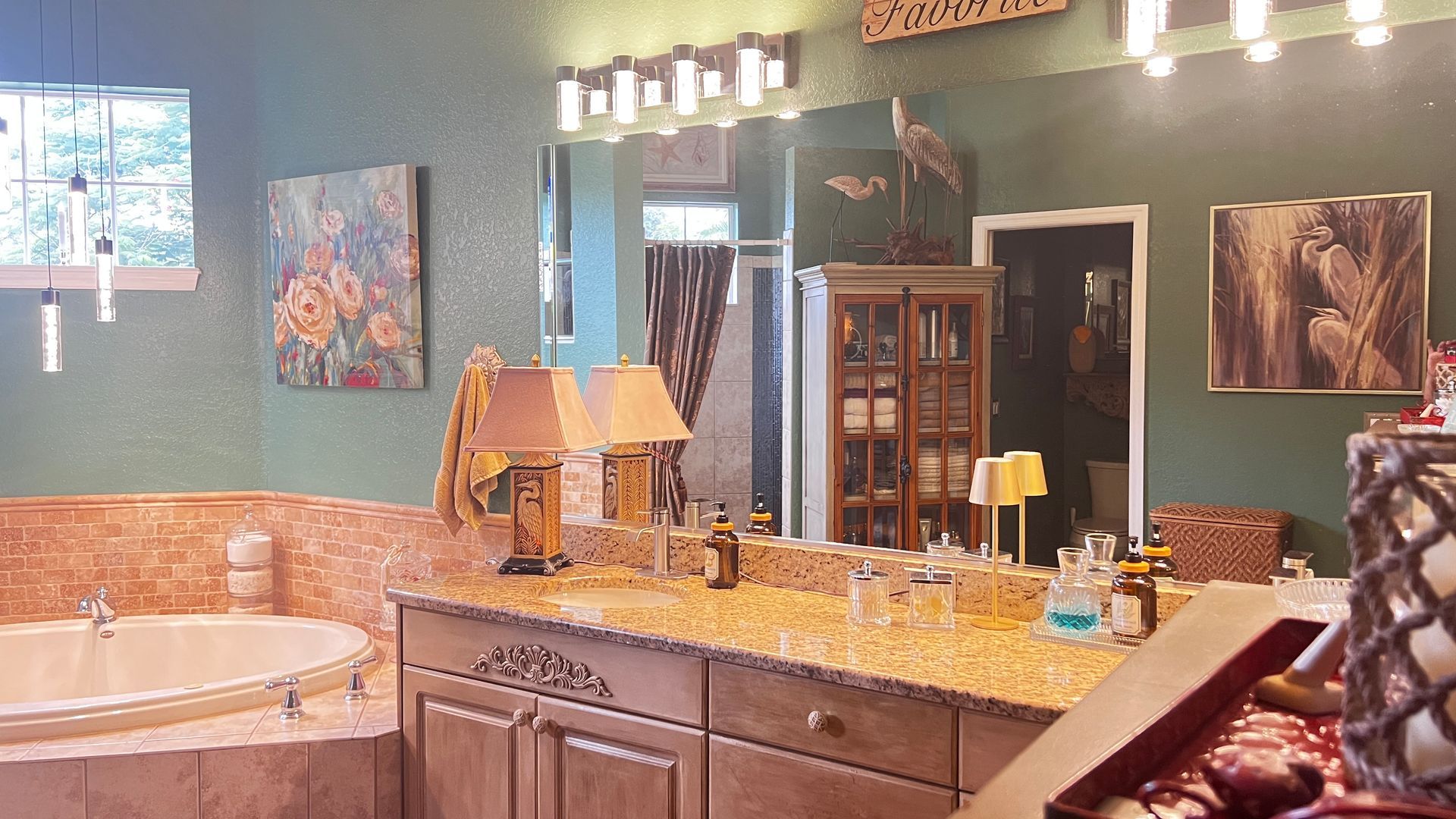 Bathroom with green walls, double sinks, large mirror, and wood cabinets lit by vanity lights.
