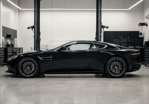 Side profile of a black Aston Martin sports coupe parked inside a clean, modern auto repair shop