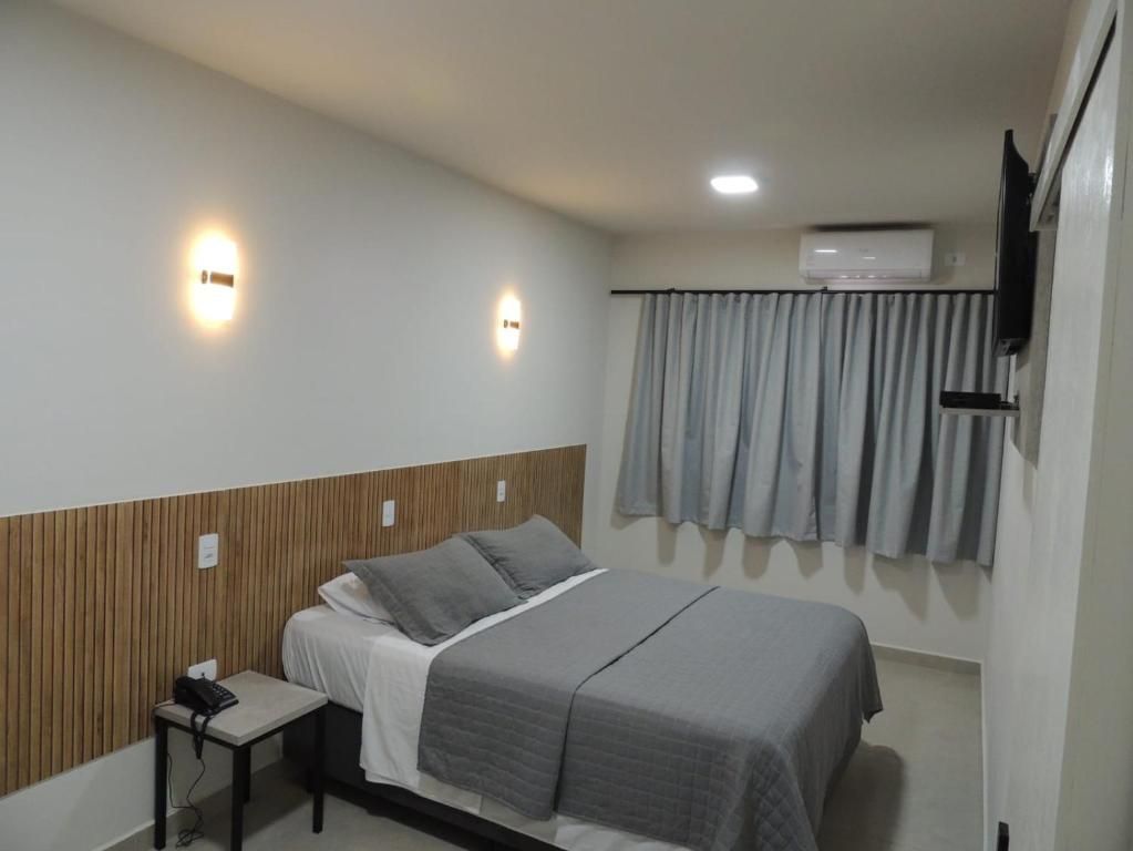 Quarto pequeno com cama arrumada, apliques de parede, cortinas e ar condicionado acima da janela.