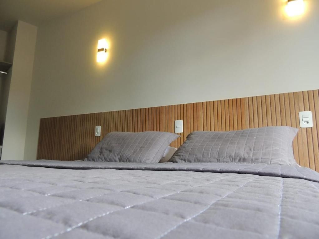 Cama arrumada com roupa de cama cinza e cabeceira de madeira em um quarto moderno.