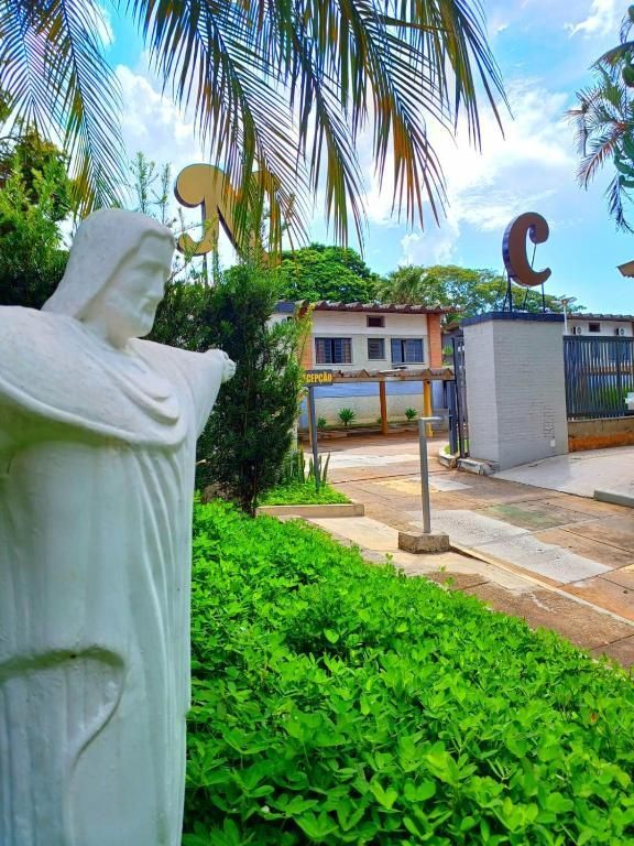 Estátua branca sob palmeiras perto da entrada de um prédio e letras de uma placa em um jardim tropical.