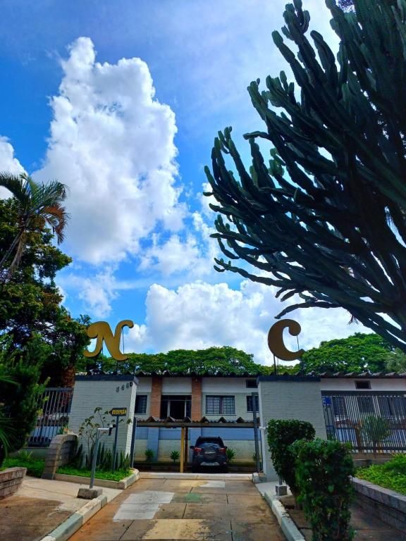 Prédio branco com portão azul sob altas árvores verdes semelhantes a cactos e um céu claro e nublado.