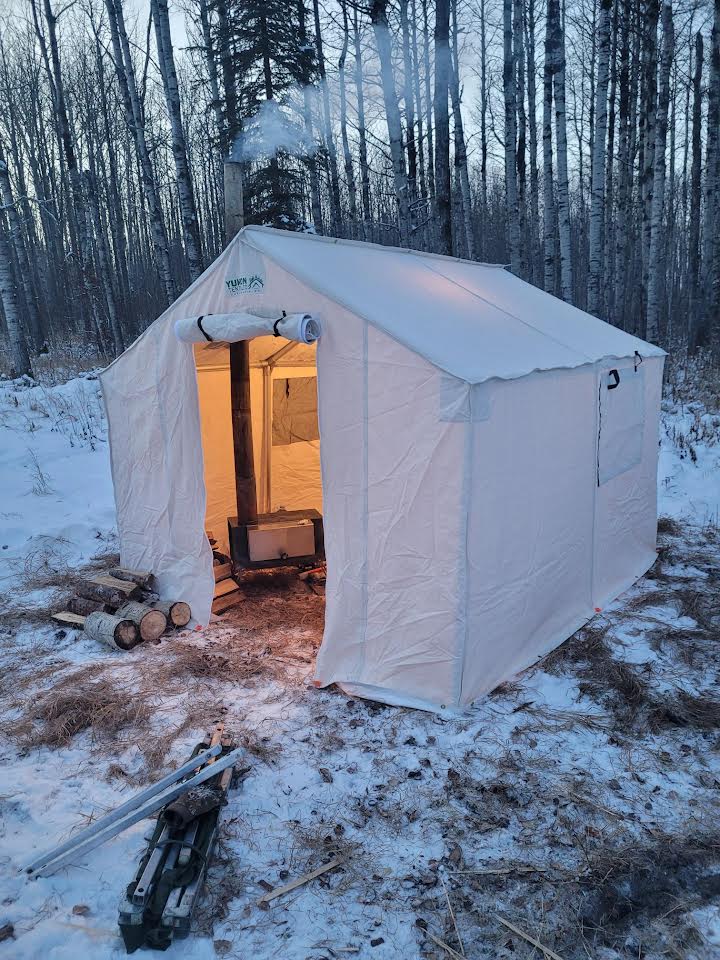 A tent is sitting in the snow in the middle of a forest.