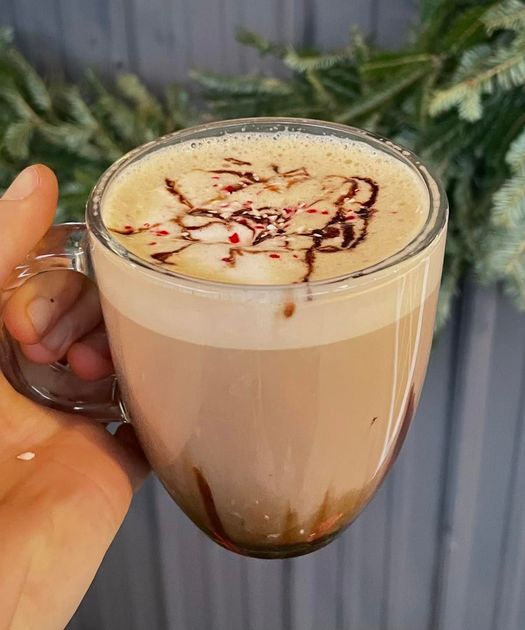 A person is holding a cup of coffee with whipped cream and chocolate shavings on top.