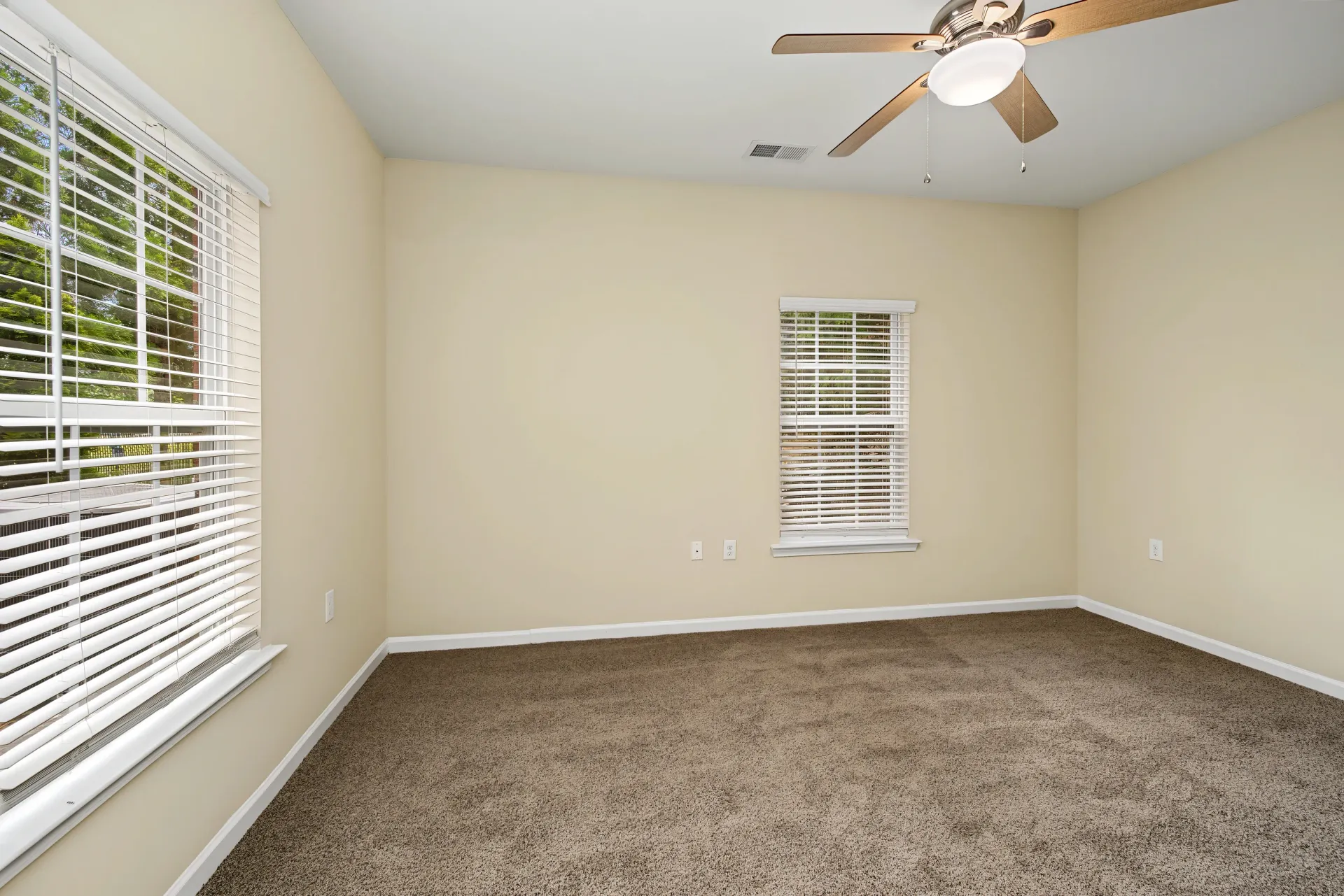 Empty bedroom with two windows and a ceiling fan.