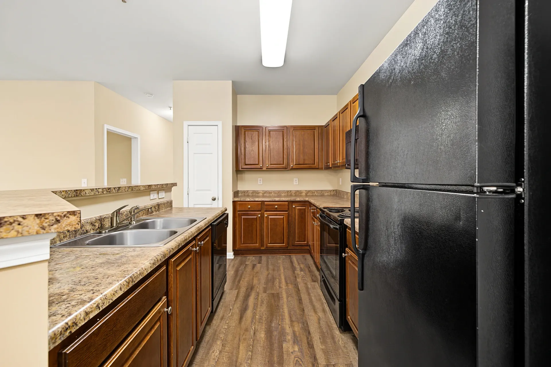 Kitchen with dark wood cabinets, granite countertops, black appliances, and stainless steel sink.